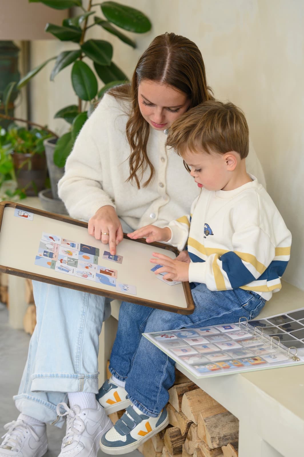 Een ouder en een kind leggen samen pictogrammen op een magneetbord. Naast hen ligt de multomap met de rest van de plaatjes.